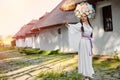 Brunette girl in a white ukrainian authentic national costume and a wreath of flowers is posing against a white hut. Royalty Free Stock Photo