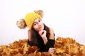 Brunette girl in yellow cap with bobbles lying on autumn leaves Royalty Free Stock Photo