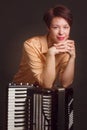 A brunette in a gold shirt, with short haircut, on a dark brownbackground of the Studio. With accordion musician