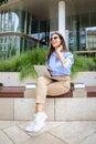 Brunette haired business woman sitting on a bench in the city and using a laptop and smartphone for work Royalty Free Stock Photo