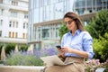 Brunette haired woman sitting on a bench in the city and using a laptop and smartphone Royalty Free Stock Photo