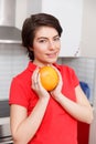 Brunette holds orange in kitchen