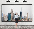 A brunette lady is pointing out the picture of New York City on the wall. Wooden floor, concrete wall and three black ceiling ligh