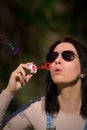 The young woman has bubble blower and she blows bubbles