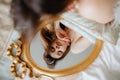 Brunette lying on bed and looking at gold-rimmed mirror. Bride holding pillow under hands and admiring reflection.