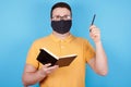 Brunette man in glasses and protection mask use pen and notebook, idea concept. Isolated on blue background