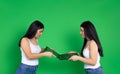 Brunette sisters share a laptop on a green background. Online earnings concept. Dividing a network digital device Royalty Free Stock Photo