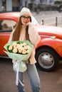 Brunette smiling woman with beautiful bouquet creamy roses flowers against the red retro car on sunny autumn day Royalty Free Stock Photo