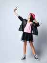 Teenage kid in black leather jacket, skirt and pink hat. She taking selfie using smartphone, posing isolated on white. Close up Royalty Free Stock Photo