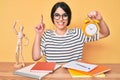 Brunette teenager girl holding alarm clock studying for exam smiling with an idea or question pointing finger with happy face,