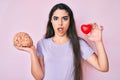 Brunette teenager girl holding brain and heart in shock face, looking skeptical and sarcastic, surprised with open mouth Royalty Free Stock Photo