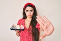 Brunette teenager girl holding cake sweets with open hand doing stop sign with serious and confident expression, defense gesture Royalty Free Stock Photo