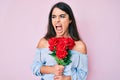 Brunette teenager girl holding flowers angry and mad screaming frustrated and furious, shouting with anger