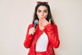 Brunette teenager girl singing song using microphone covering mouth with hand, shocked and afraid for mistake Royalty Free Stock Photo