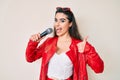 Brunette teenager girl singing song using microphone smiling happy and positive, thumb up doing excellent and approval sign Royalty Free Stock Photo