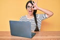 Brunette teenager girl working using computer laptop smiling happy doing ok sign with hand on eye looking through fingers Royalty Free Stock Photo