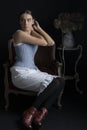 A Victorian woman wearing a corset and combinations and sitting on a chair in front of a dark backdrop Royalty Free Stock Photo