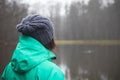 Brunette in winter jacket looking at a small pond near Opava, Czech Republic. Green and blue winter jacket. Lifestyle