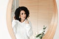 A brunette woman with African curls looks in the mirror and straightens her hair