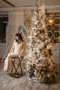 A brunette woman in a beautiful light tight dress next to a Christmas tree. The magical atmosphere of Christmas Eve on Royalty Free Stock Photo