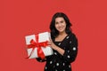 Brunette woman in a black dress smiling holding Christmas giftbox of white color with red ribbon. Royalty Free Stock Photo