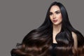 Brunette woman with black wavy ombre hair. Portrait on a gray background