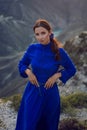 brunette woman in a blue long dress stands on the edge of the Sulak canyon in the evening