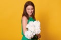 Brunette woman with charming smile wearing green dress, holding bouquet of white peonies and looking at flowers with gentle, Royalty Free Stock Photo