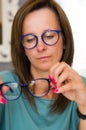 Brunette woman choosing and buying eyeglasses in optician salon or shop