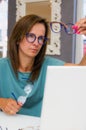 Brunette woman choosing and buying eyeglasses in optician salon or shop