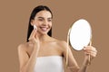 Brunette woman cleansing face with cotton pad, looking at mirror Royalty Free Stock Photo