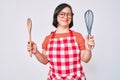 Brunette woman with down syndrome cooking using baker whisk and spoon winking looking at the camera with sexy expression, cheerful Royalty Free Stock Photo