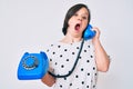 Brunette woman with down syndrome holding vintage telephone afraid and shocked with surprise and amazed expression, fear and Royalty Free Stock Photo