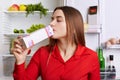 Brunette woman drinks milk from papaer container, feels fresh and healthy as eats nutritious food, stands near fridge with product Royalty Free Stock Photo
