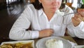 Brunette woman eating rice in a cafe. On the table meat with vegetables