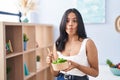 Brunette woman eating a salad at home making fish face with mouth and squinting eyes, crazy and comical