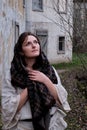 Brunette woman in headscarf and vintage dress on the background of old houses. Girl on the background of a gloomy autumn landscape