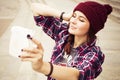 Brunette woman in hipster outfit sitting on steps and taking selfie on retro camera on the street. Toned image Royalty Free Stock Photo