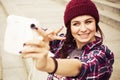 Brunette woman in hipster outfit sitting on steps and taking selfie on retro camera on the street. Toned image Royalty Free Stock Photo