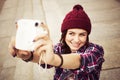 Brunette woman in hipster outfit sitting on steps and taking selfie on retro camera on the street. Toned image Royalty Free Stock Photo