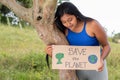 A brunette woman holds a sign calling to save the planet as she reads it. Latina girl protects nature and trees. Royalty Free Stock Photo