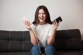 Brunette woman looks angry holding smartphone in one hand and portative battery charger in another sitting on the sofa in her