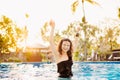 Brunette woman making water splash in bikini at the pool. Slim fit tanning woman having fun in pool