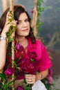 a brunette woman in a pink blouse with peonies on the swing.