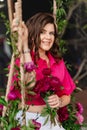 a brunette woman in a pink blouse with peonies on the swing.