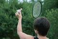 Brunette woman plays badminton outdoors holding shuttlecock and a racket in her hands