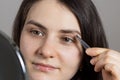 A brunette woman plucked her eyebrows in front of a mirror. Correction of the shape of the eyebrow with tweezers on your Royalty Free Stock Photo