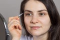 A brunette woman plucked her eyebrows in front of a mirror. Correction of the shape of the eyebrow with tweezers on your Royalty Free Stock Photo
