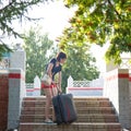 A brunette woman in red shorts hardly lifts a large heavy suitcase steps at the train