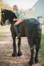 Brunette woman riding dark horse at summer green forest. Royalty Free Stock Photo